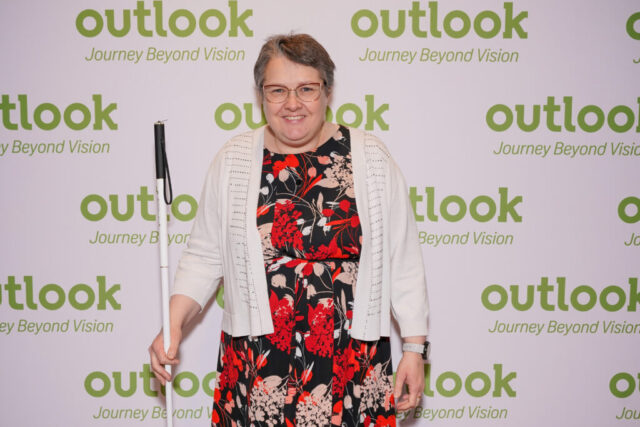 Sam is smiling in front of an Outlook backdrop.