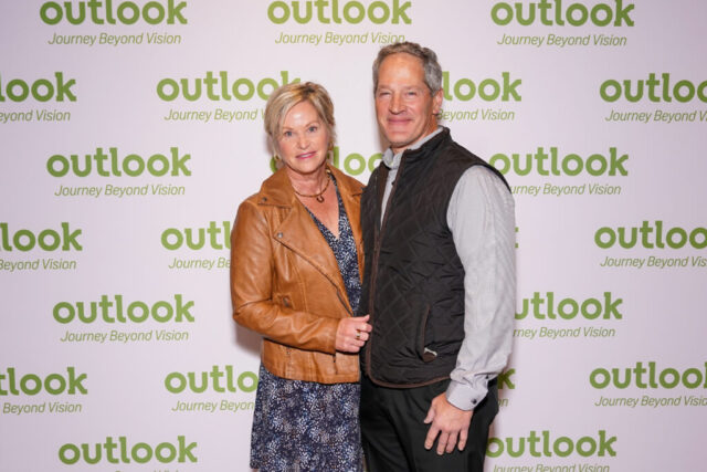 A man and woman smiling in front of an Outlook backdrop.