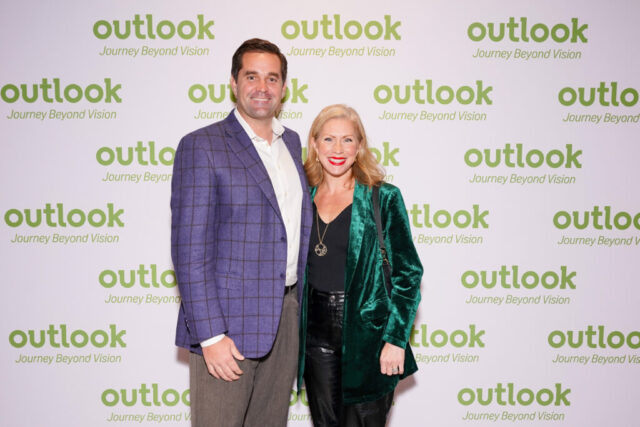 A man and woman smiling in front of an Outlook backdrop.