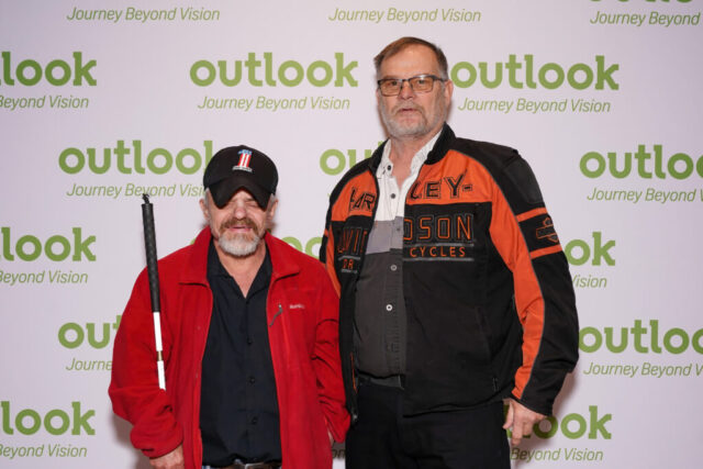 Monty and a male guest are smiling in front of an Outlook backdrop.