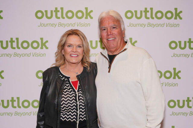 A man and woman smiling in front of an Outlook backdrop.