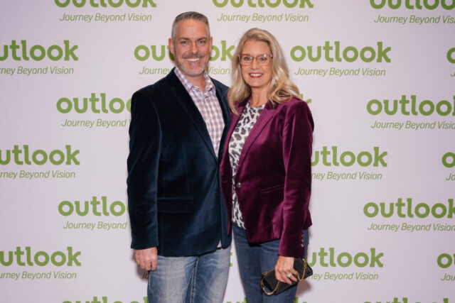 A man and woman smiling in front of an Outlook backdrop.