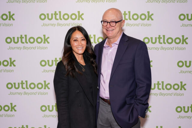 Gary and a woman are smiling in front of an Outlook backdrop.