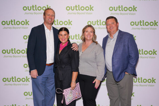 Two man and woman pairs are smiling in front of an Outlook backdrop.