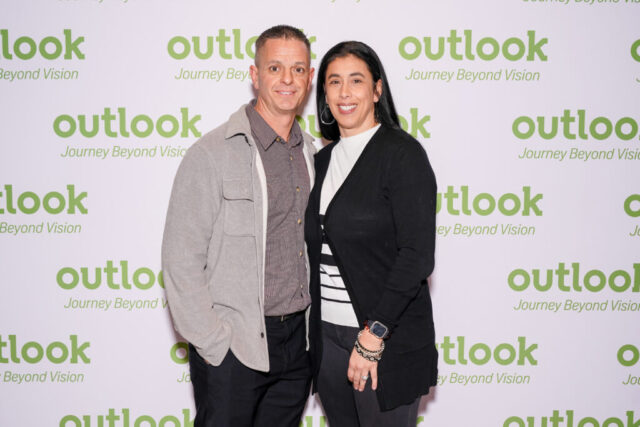 Annie and a male guest are smiling in front of an Outlook backdrop.