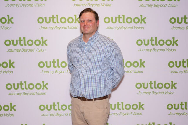 A man smiling in front of an Outlook backdrop.