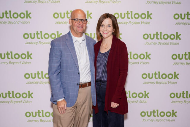 Bill and his wife are smiling in front of an Outlook backdrop.