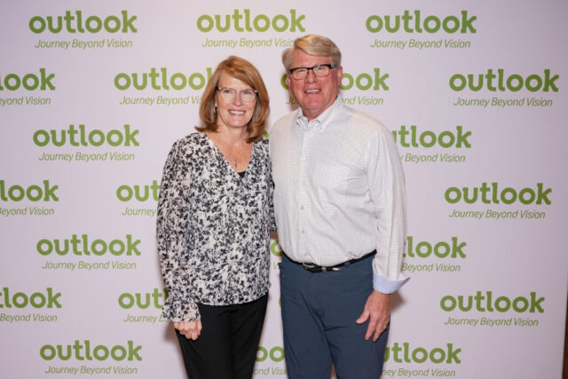 Rick and a female guest smiling in front of an Outlook backdrop.
