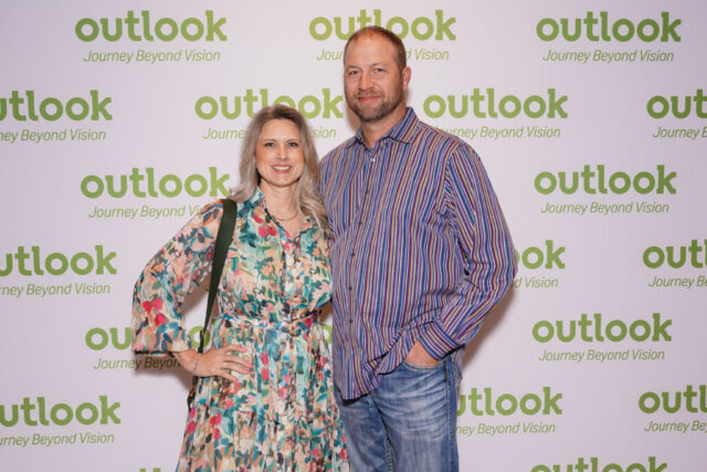 A man and woman smiling in front of an Outlook backdrop.