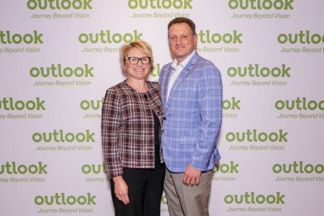 James and a female guest are smiling in front of an Outlook backdrop.