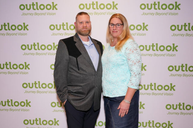 Kenneth and a female guest are smiling in front of an Outlook backdrop.