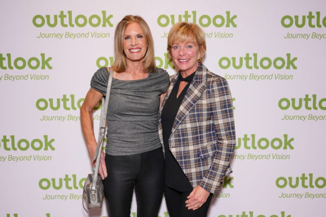 Two women are smiling in front of an Outlook backdrop.