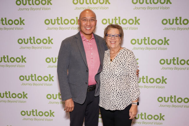 A man and woman smiling in front of an Outlook backdrop.
