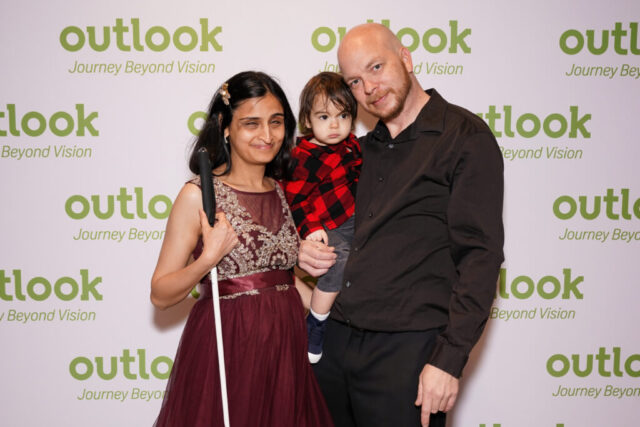 Dave, wife, and child are smiling in front of an Outlook backdrop.