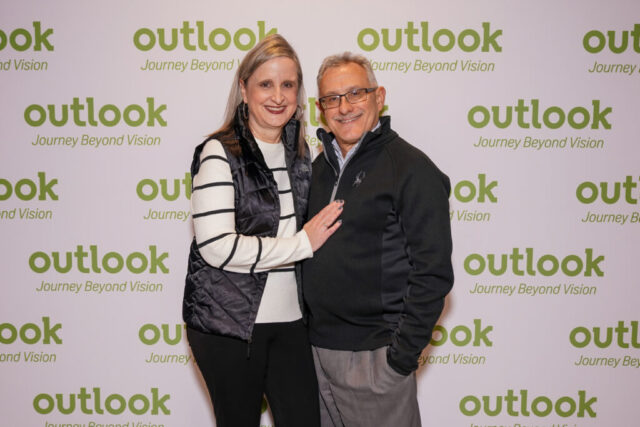 A man and woman smiling in front of an Outlook backdrop.
