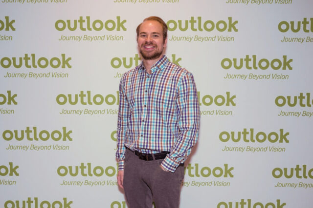 Kyle is smiling in front of an Outlook backdrop.
