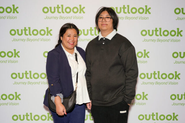 Neri and a man are smiling in front of an Outlook backdrop.