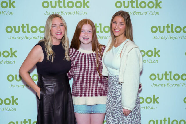 Cassie and two ladies are smiling in front of an Outlook backdrop.