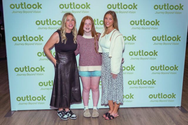 Cassie and two ladies smiling in front of an Outlook backdrop.