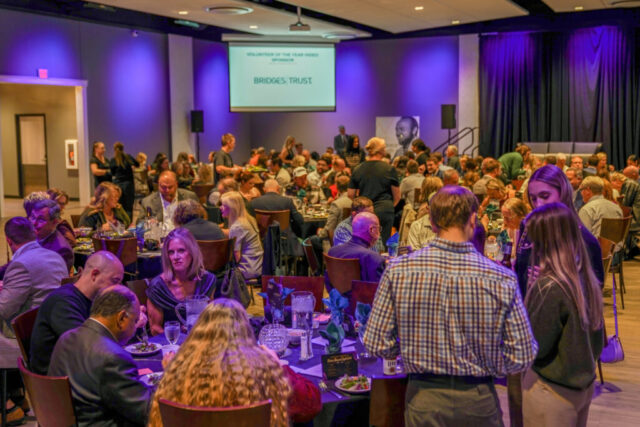 An overview shot of the room. Guests are eating dinner at their tables and talking.