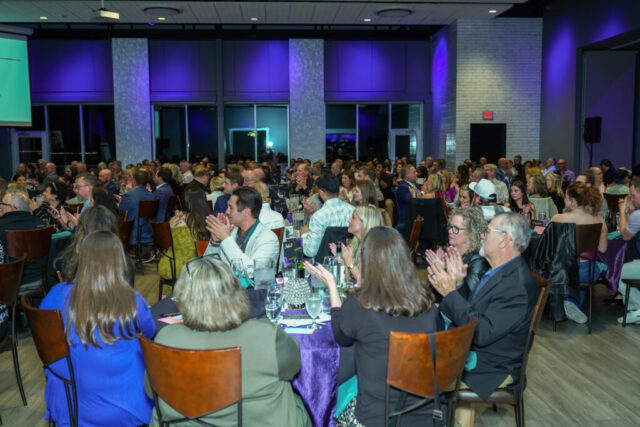 Guests are seated at their tables and clapping.