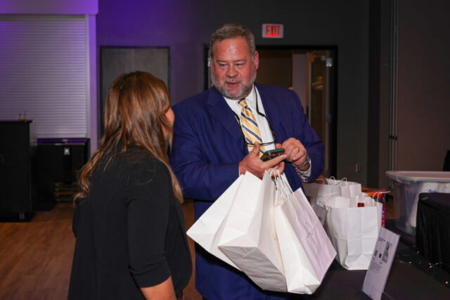 A man holding his auction items talking to a volunteer.