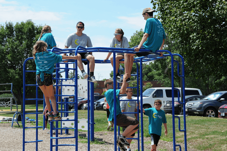 Group shot of campers and volunteers sitting on top of a park's jungle gym.