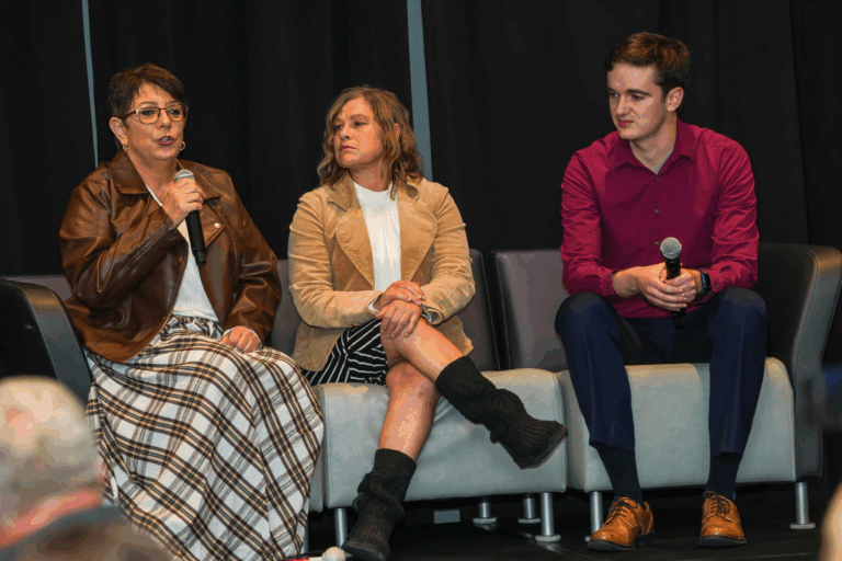 Rondae, Megan, and Isaac are sitting on a couch on stage at VBS. Rondae is speaking.