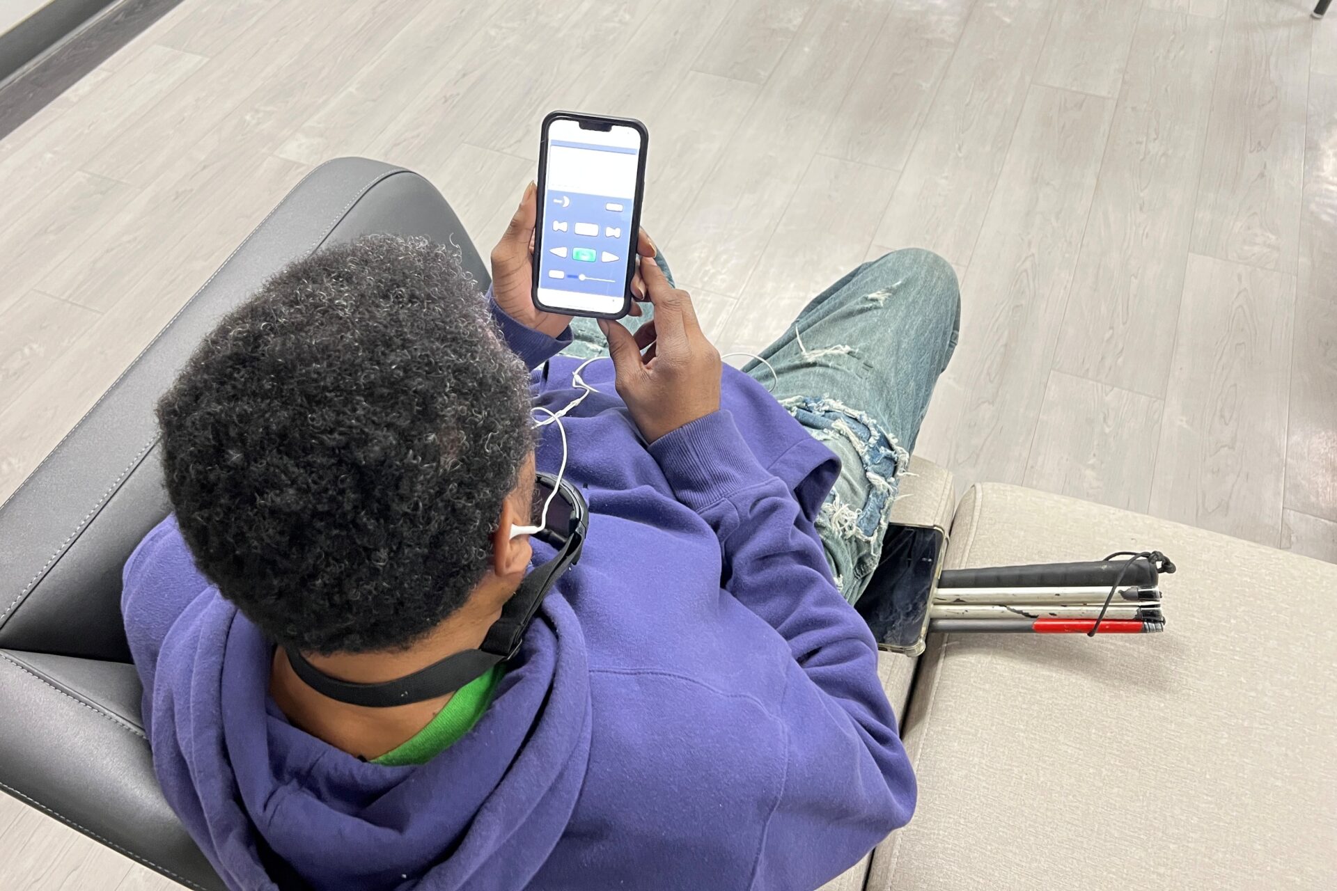 Alex sitting on a couch with headphones and the BARD mobile audio book app pulled up on his phone.