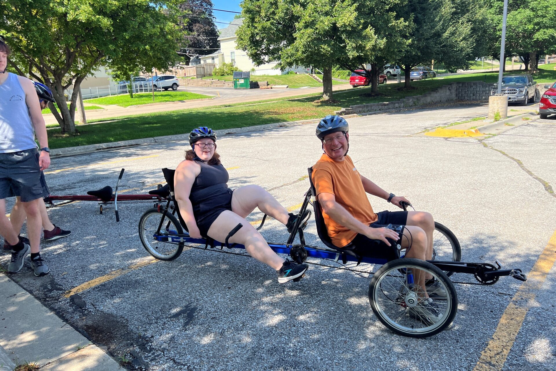 Corey in the front seat of a recumbent and Milla in the back seat wearing helmets and getting ready to take off for a ride