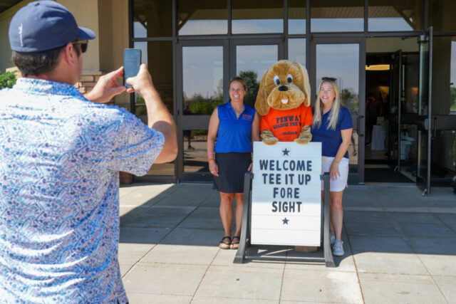 Nina, Cassie, and Fenway in front of the Tee It Up Fore Sight sign.