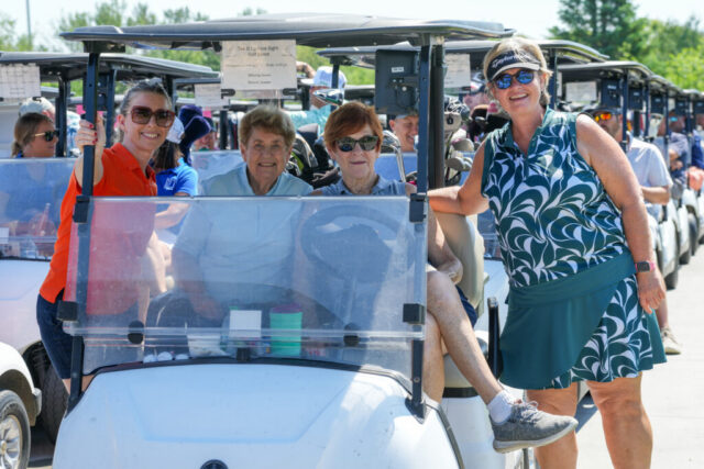 4 ladies smiling in and by their golf cart.
