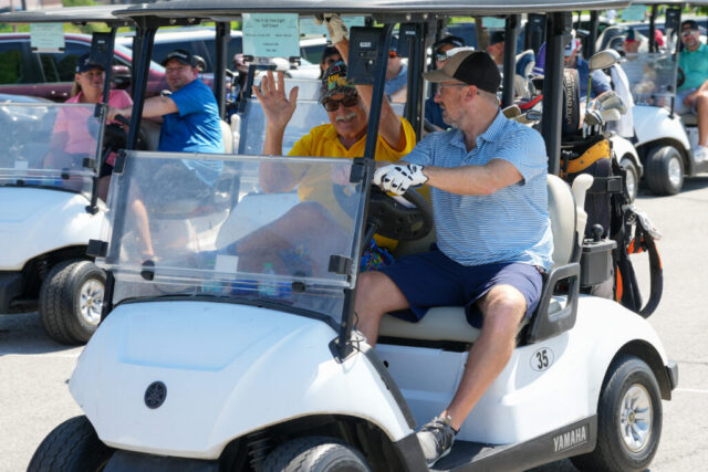 Two men in their golf cart. The one on the left is waving at the camera.