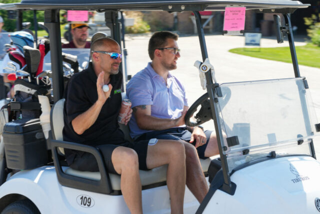 Nick C and another man riding on their golf cart.