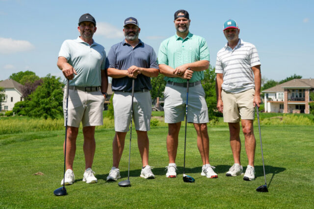 Four gentlemen are smiling on the green for a group photo.