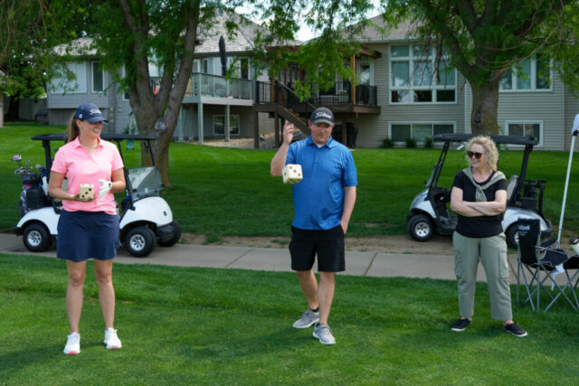 Ashley and a man are holding die while Dana watches.