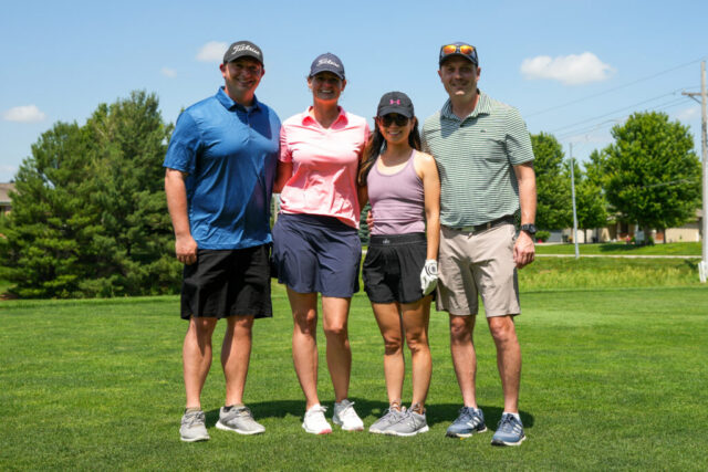 Two men and two ladies are smiling on the green for a group photo.