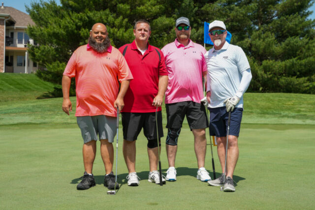 Four gentlemen are smiling on the green for a group photo.