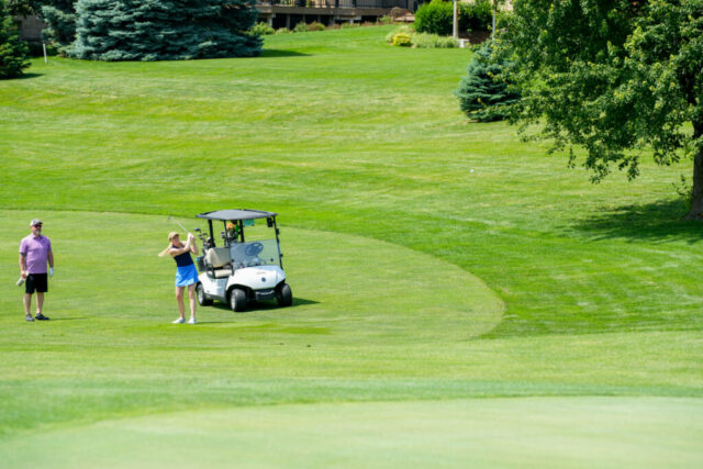 A woman just swung her club and a man watches behind her.