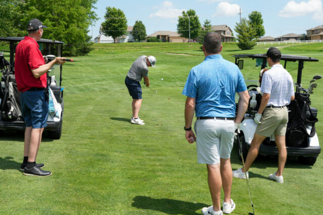 A man is swinging his club on the green while three others watch.
