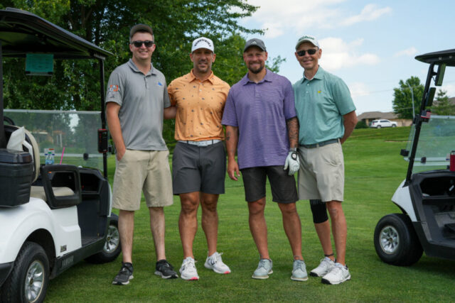 Four gentlemen are smiling on the green for a group photo.