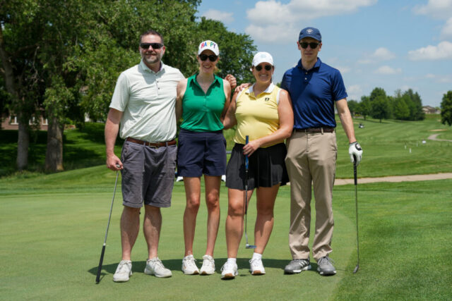 Two men and two women are smiling on the green for a group photo.