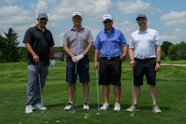 Four gentlemen are smiling on the green for a group photo.