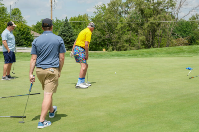 A man is watching his ball and two others watch behind him.