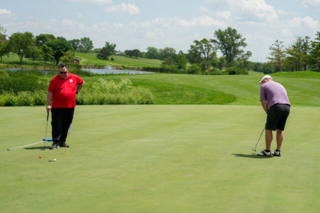 Two men on the green. One is putting and one is watching.