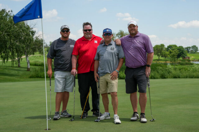 Four gentlemen are smiling on the green for a group photo.