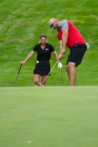 A man is mid swing while a woman watches behind him.