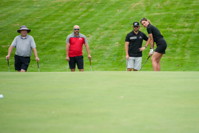 A lady is getting ready to swing while three men watch behind her.