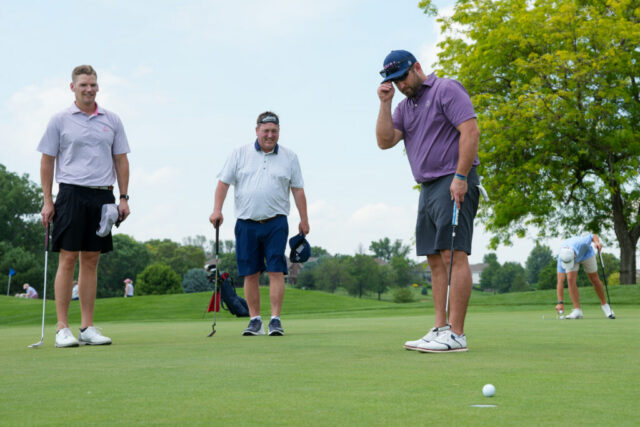 3 men watching a ball on the green.