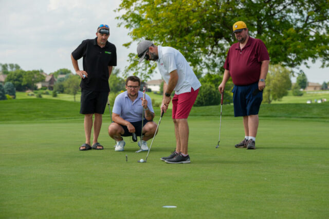 A man is putting with sleep shades on while three others watch behind him.